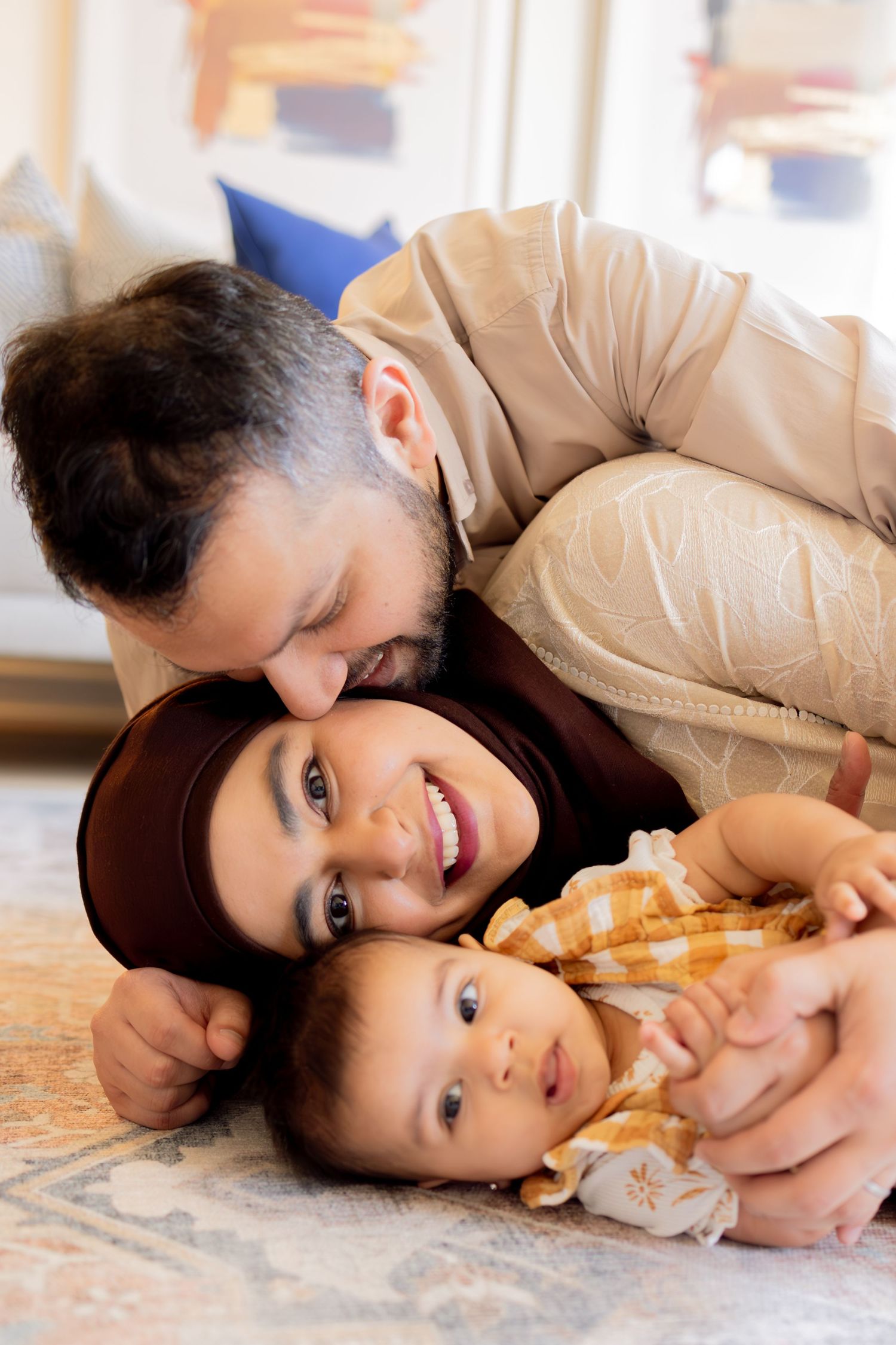 A couple in beige clothing lies together on a wooden floor in a sequence of tender, playful poses.