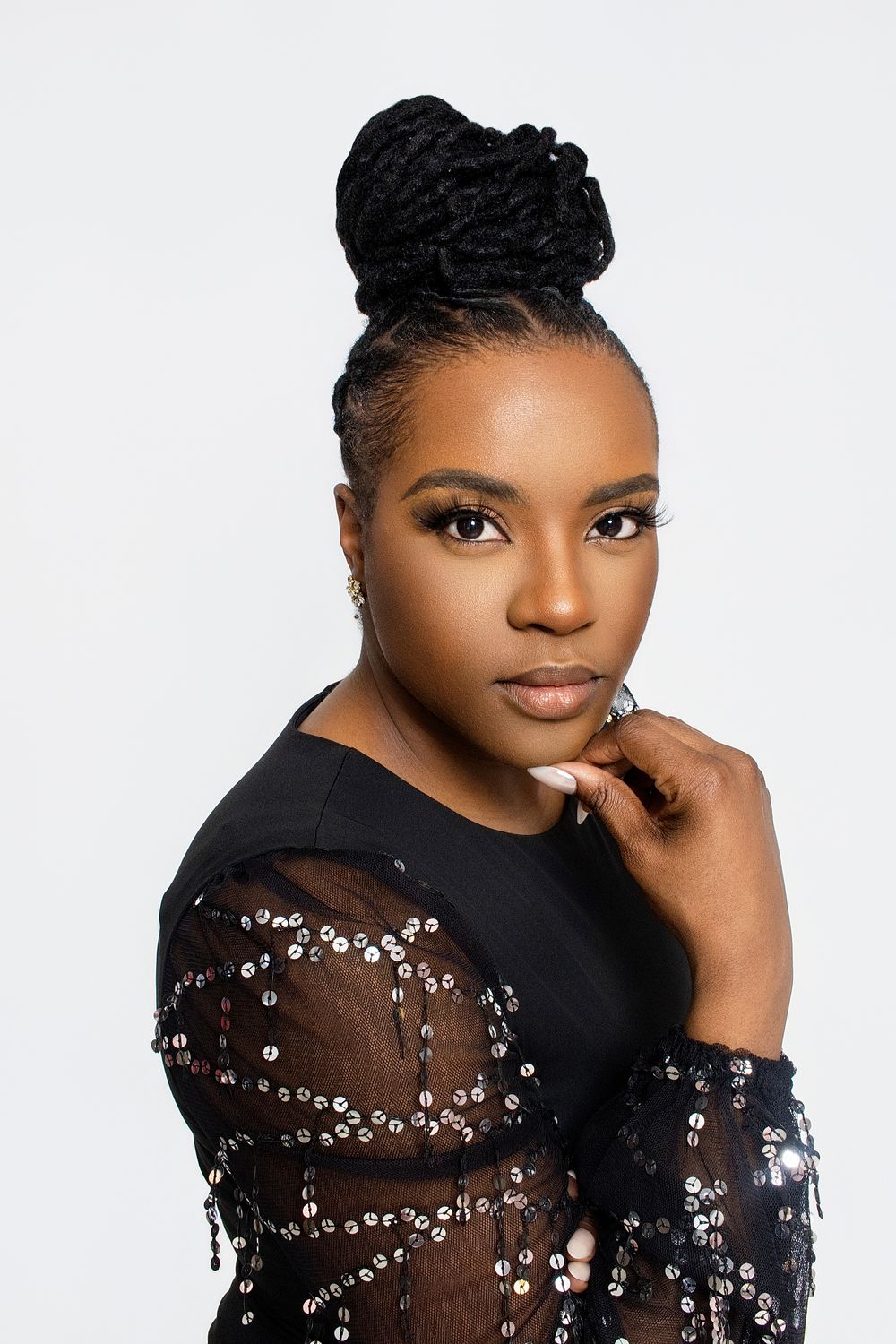 Elegant portrait featuring someone in a black sheer embellished top against white background.