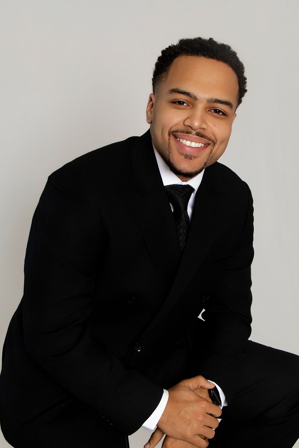 Professional portrait series showing someone in a black suit and tie against a light gray background.