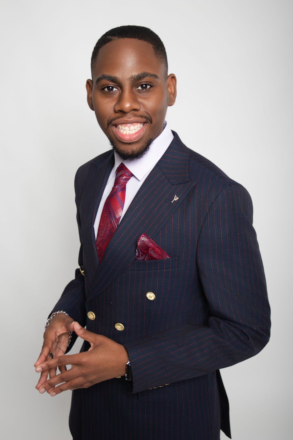 Professional portraits in pinstripe suit with red tie and pocket square against white backdrop.