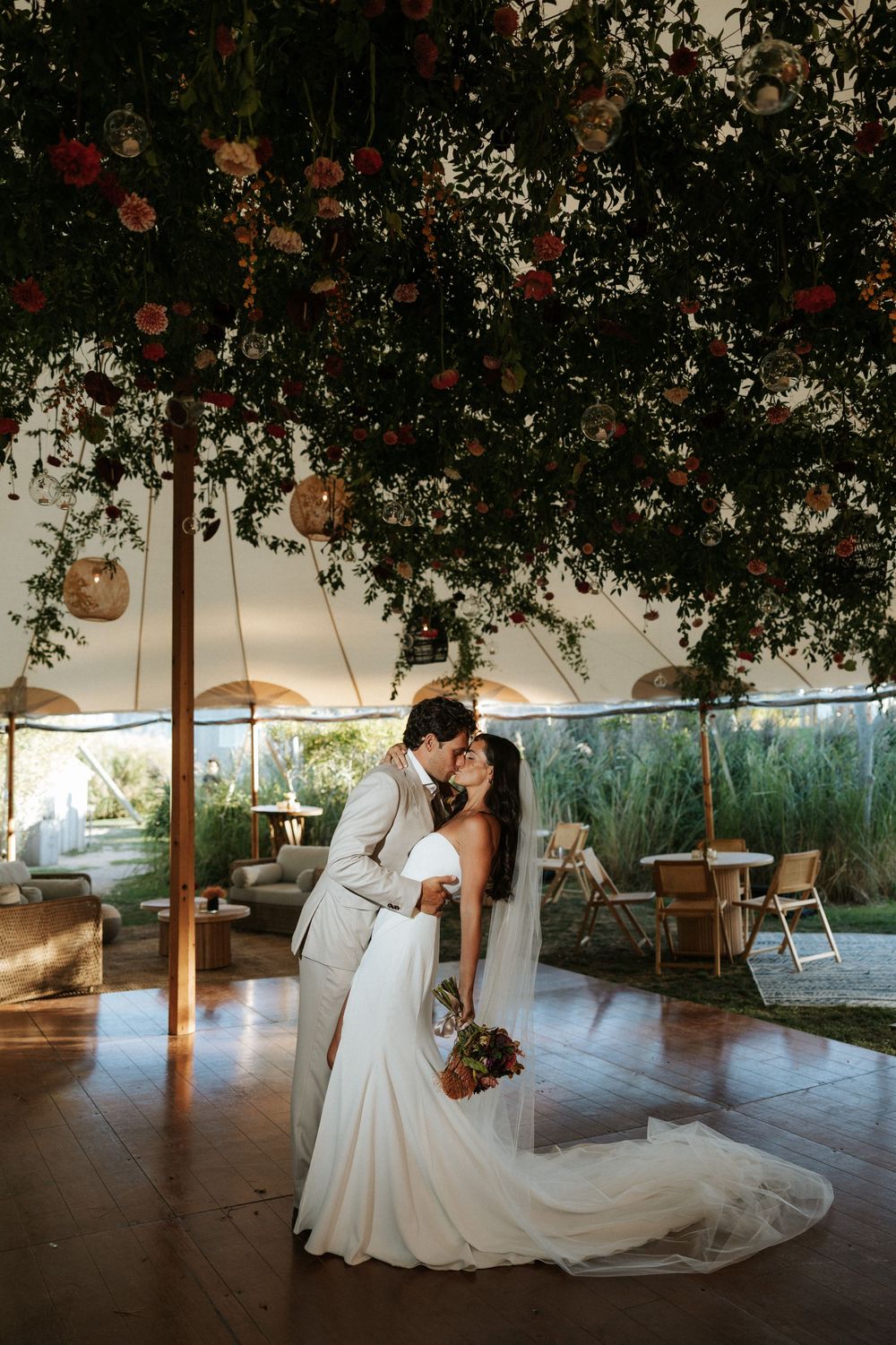 Newlyweds kiss under hanging greenery in The Crow's Nest wedding reception tent