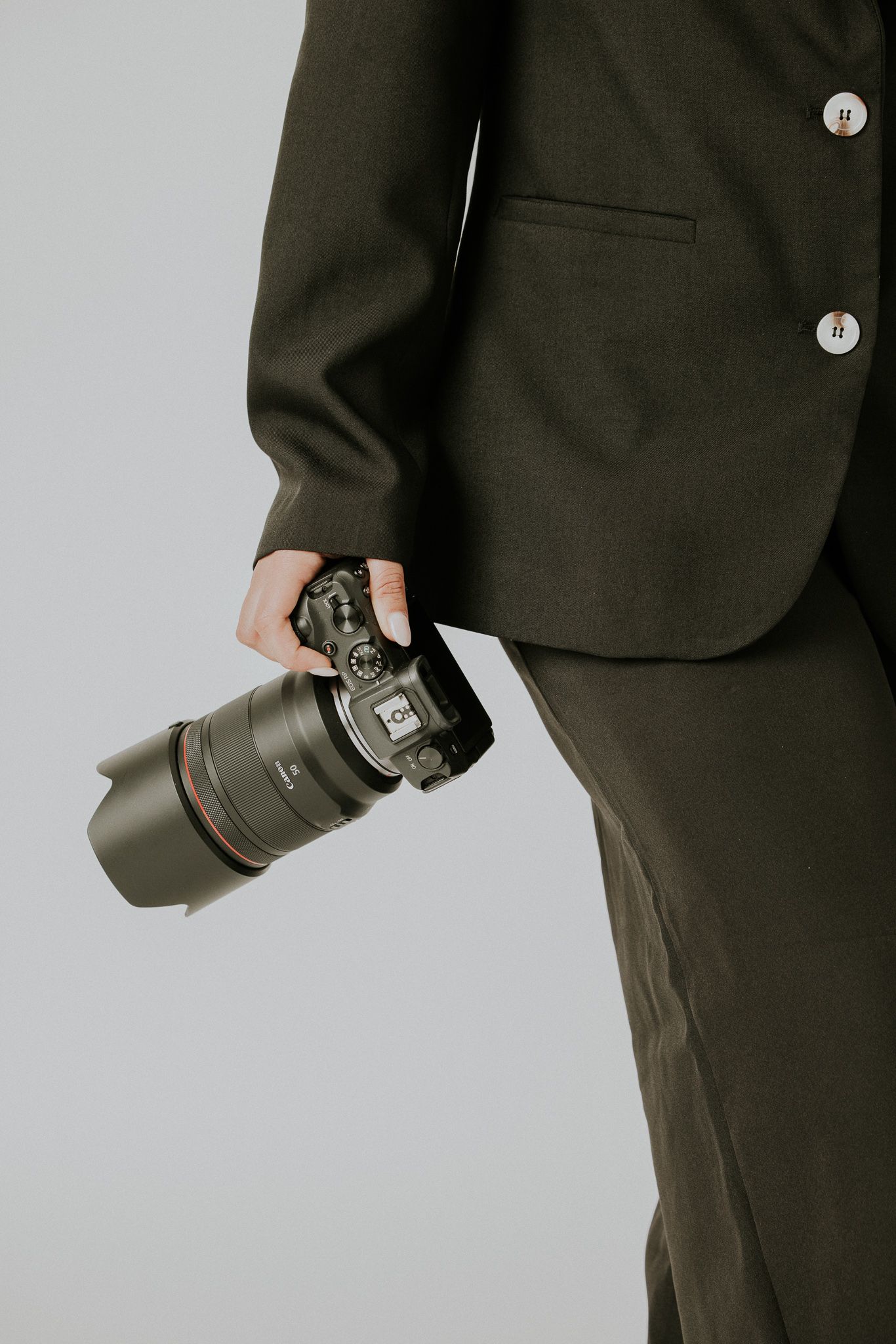 Professional photographer in dark suit jacket holding camera lens against light gray studio background.