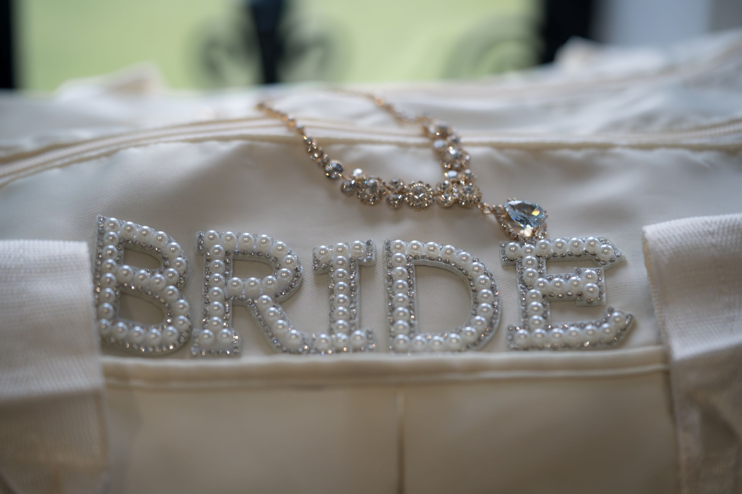 A close-up of a rhinestone 'BRIDE' accessory on white fabric with delicate crystal details.