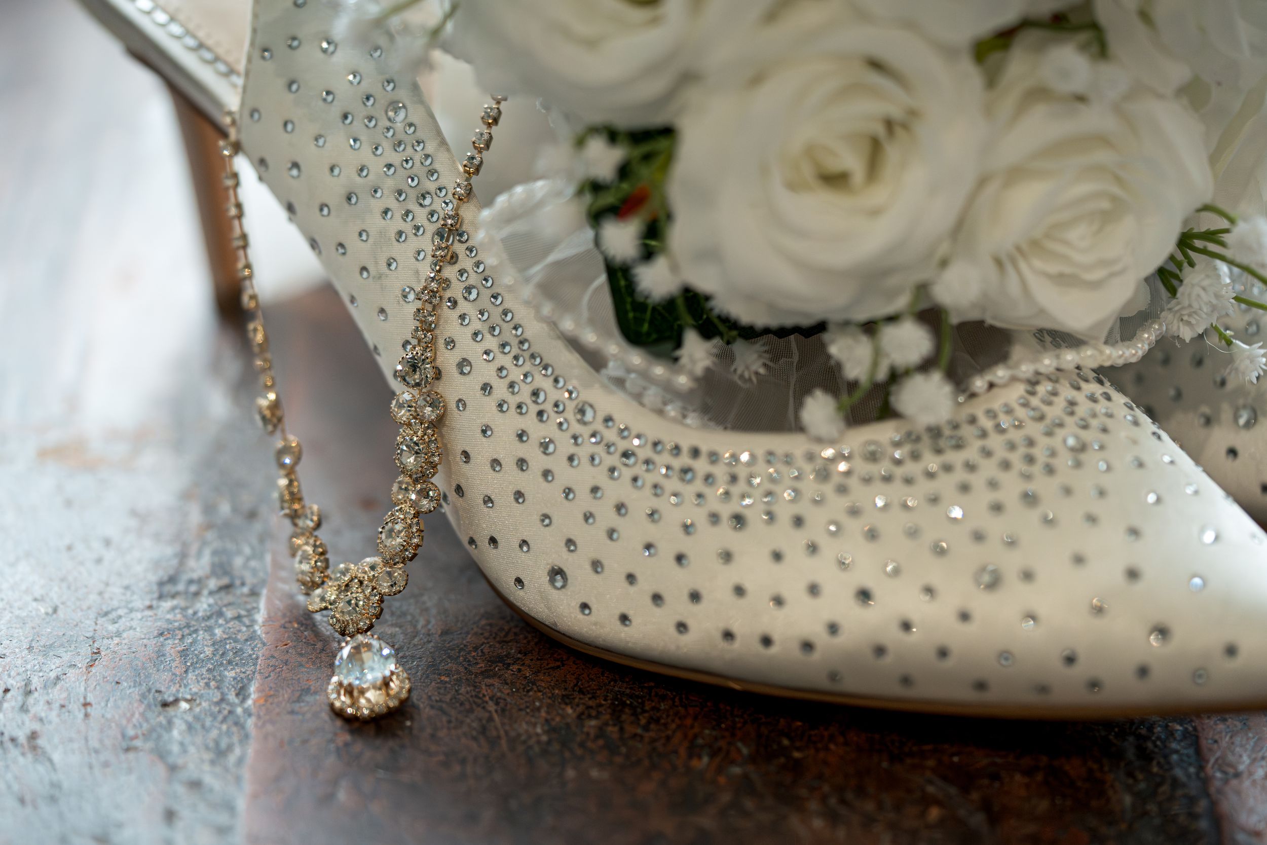 Wedding detail shot featuring white roses and a sparkly bridal shoe with crystal embellishments.