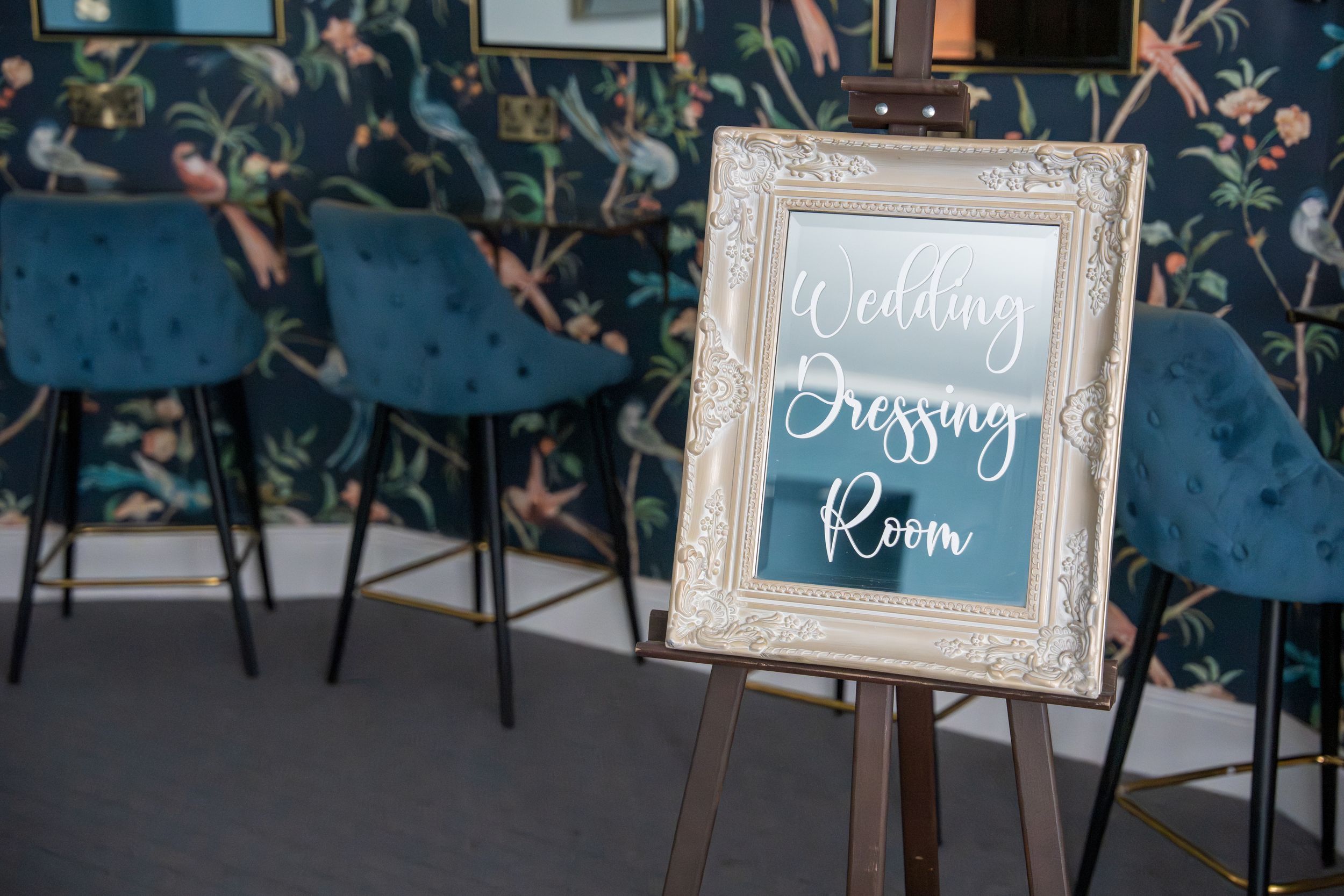 Elegant wedding reception venue setup with ornate frames displaying signage and blue velvet chairs.