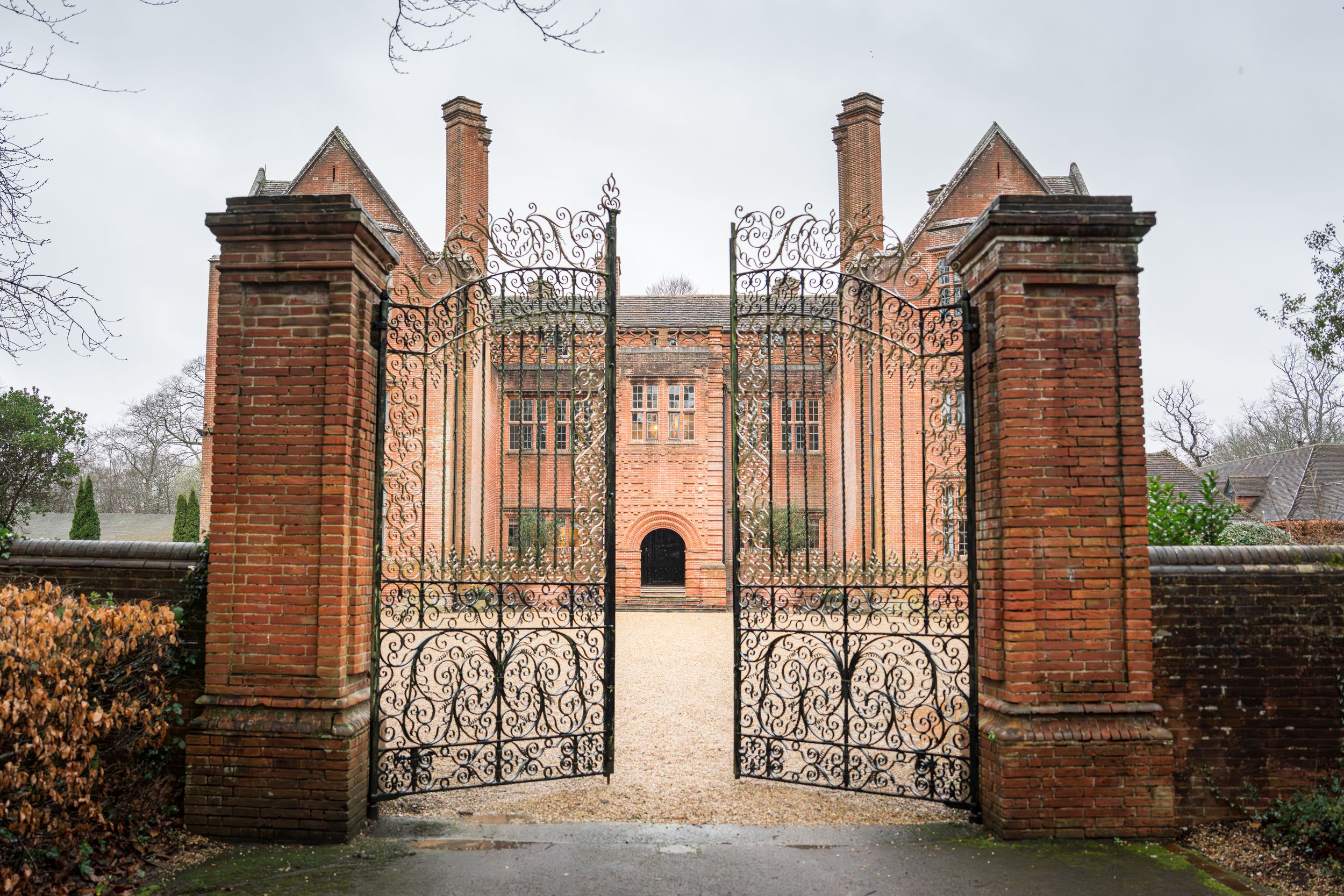 Ornate brick entrance gates with decorative ironwork and pillars lead to a formal garden or estate property.