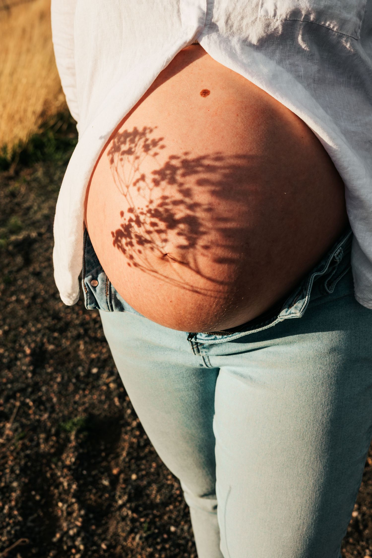 Pregnant woman's bare belly with beautiful floral shadow pattern outdoors |Maternity Photos in Boulder Colorado
