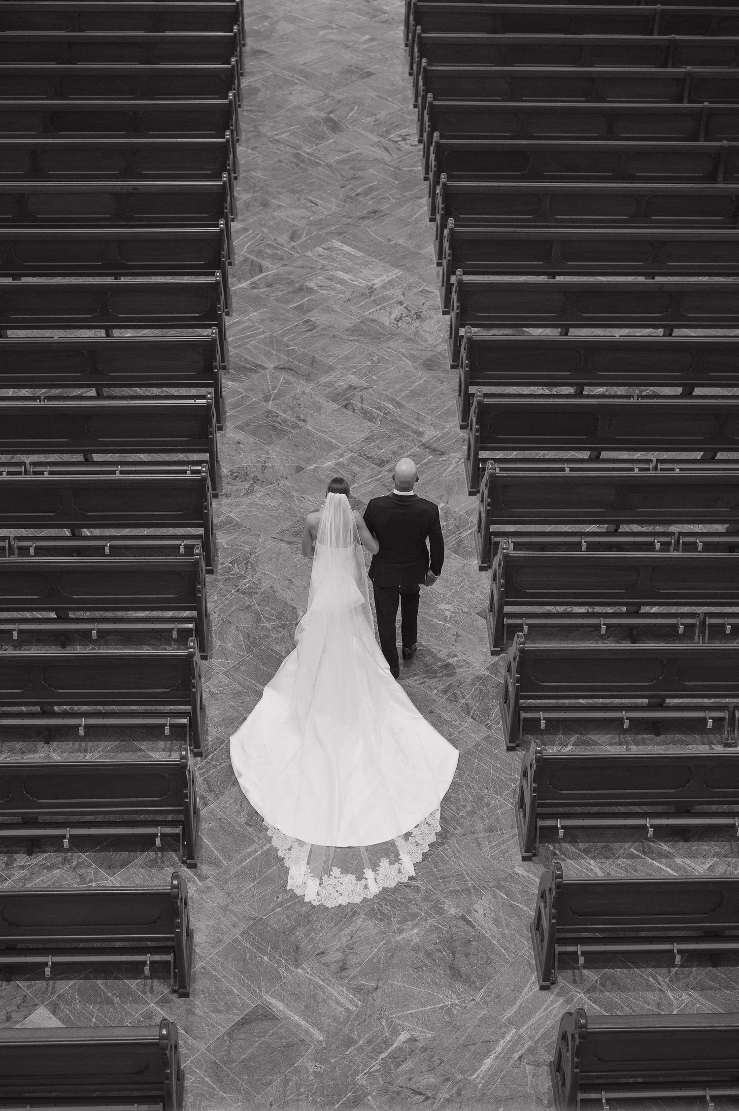 Black and white photo showing wedding party members' formal attire and white bouquets at an elegant reception venue.