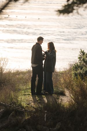 Two silhouetted figures stand together against a bright sky on a grassy hillside at sunset.