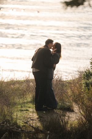 Silhouetted couple sharing an intimate moment at sunset on a grassy coastal cliff overlooking the ocean.