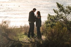 A couple stands silhouetted against a scenic natural backdrop during golden hour at a scenic overlook.