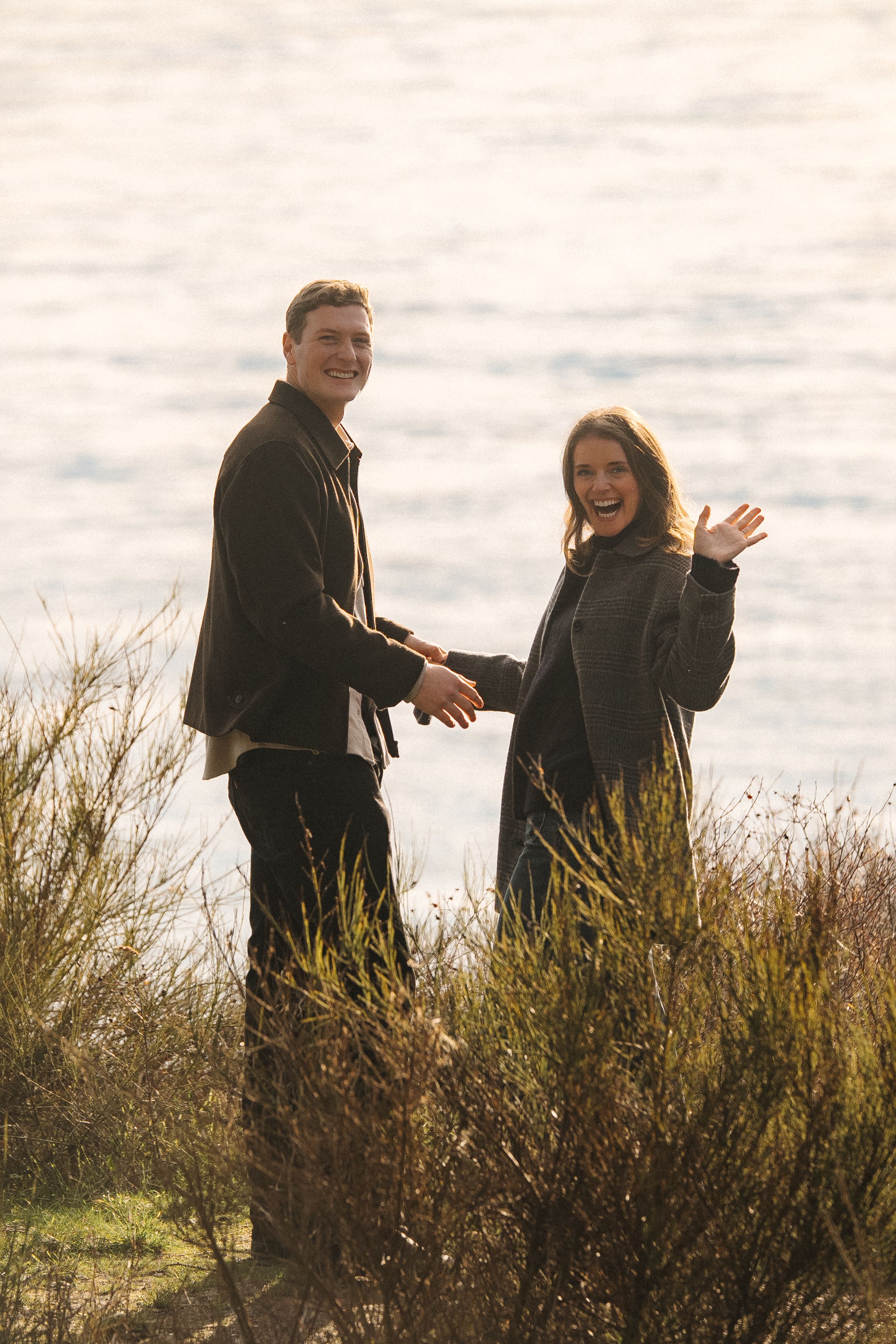 A couple shares a joyful moment together while standing in tall grass on a cloudy day.