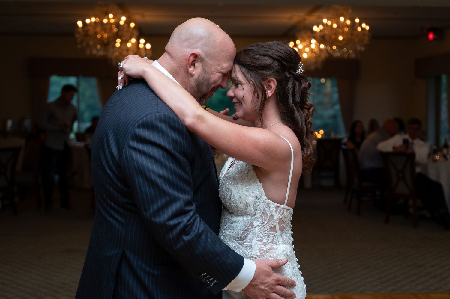 A couple shares a romantic dance together at their wedding reception under warm chandelier lighting.