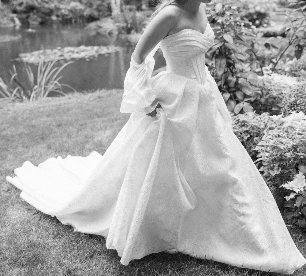 Wedding dress details showing flowing white fabric and train in an outdoor garden setting.
