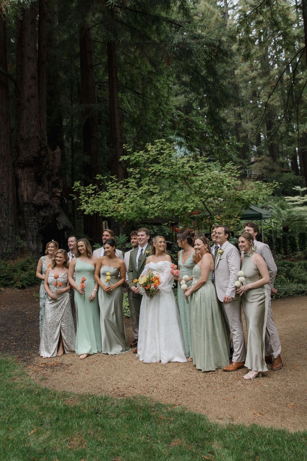Wedding party in mint green and neutral dresses poses together on a forest path.