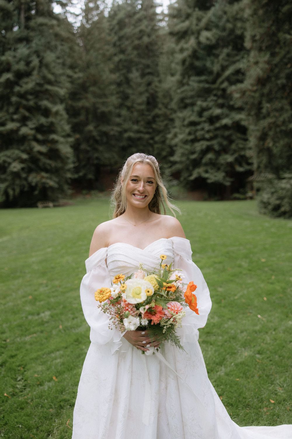Outdoor bridal portrait in a white gown holding a vibrant bouquet against a backdrop of evergreen trees.