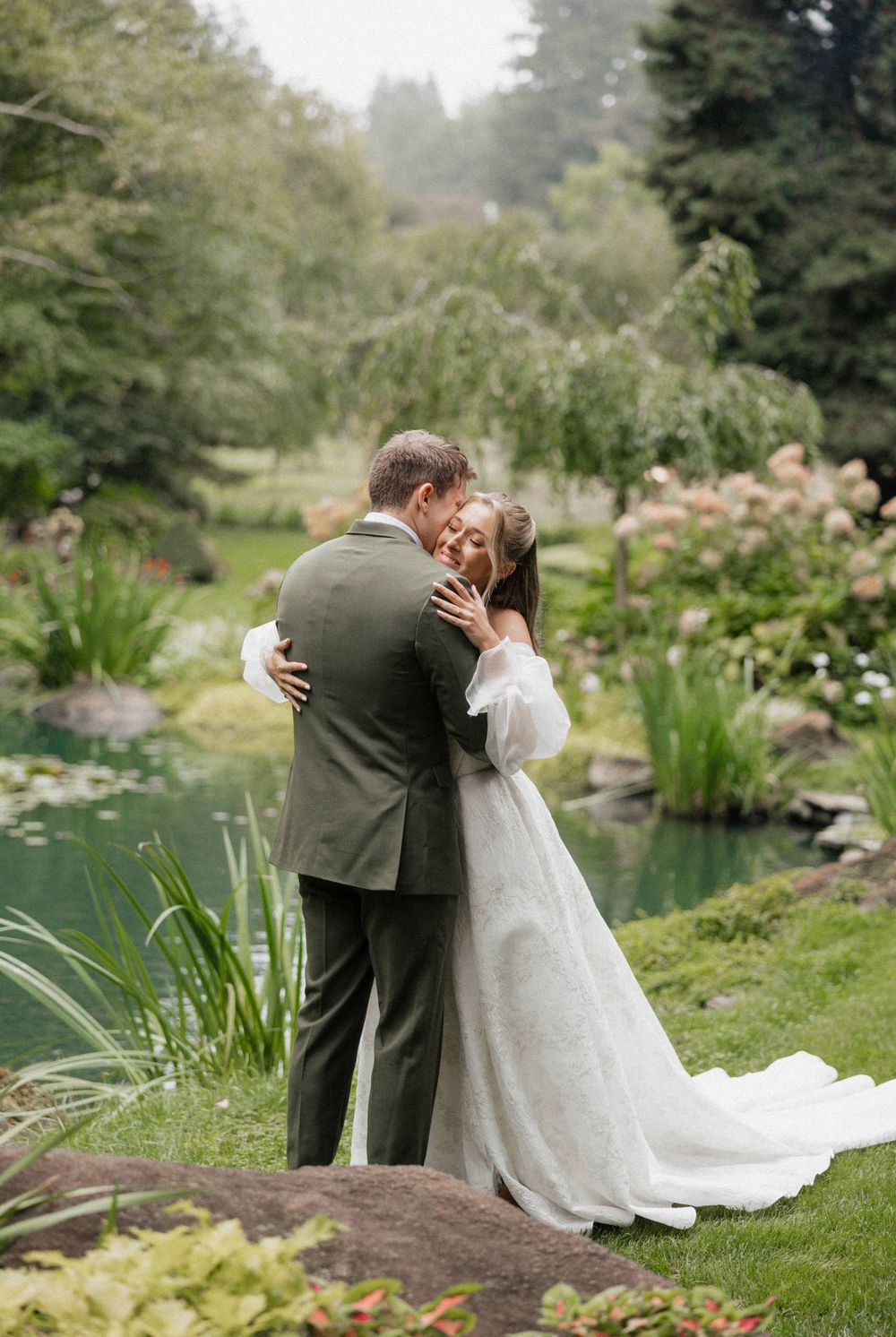 A couple shares a romantic moment by a serene pond surrounded by lush gardens and greenery.