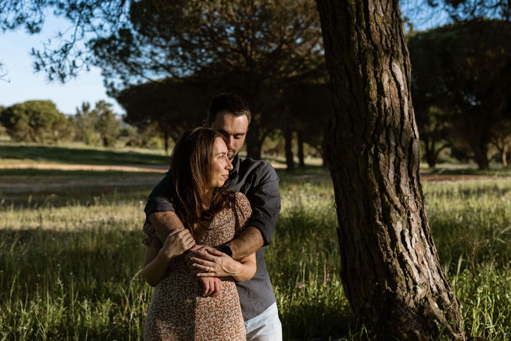 Couple embracing near tree in soft golden light during pre wedding photoshoot in Sesimbra pine forest Portugal