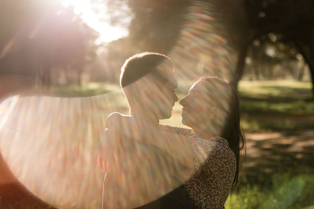 Black dog sitting in grass during couple photoshoot in Sesimbra with couple blurred in foreground