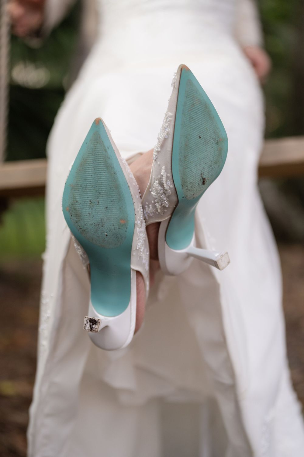 Bride displays her something blue Betsey Johnson wedding heels with teal soles while seated on a swing.