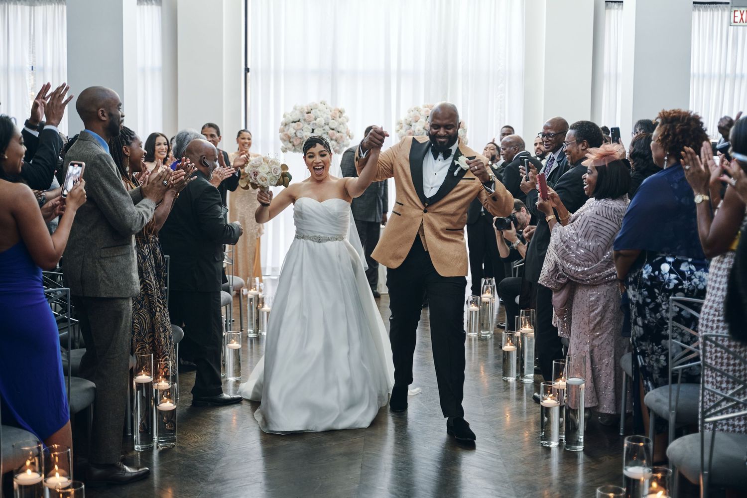 Wedding guests form lines on dance floor during reception celebration at elegant white venue.