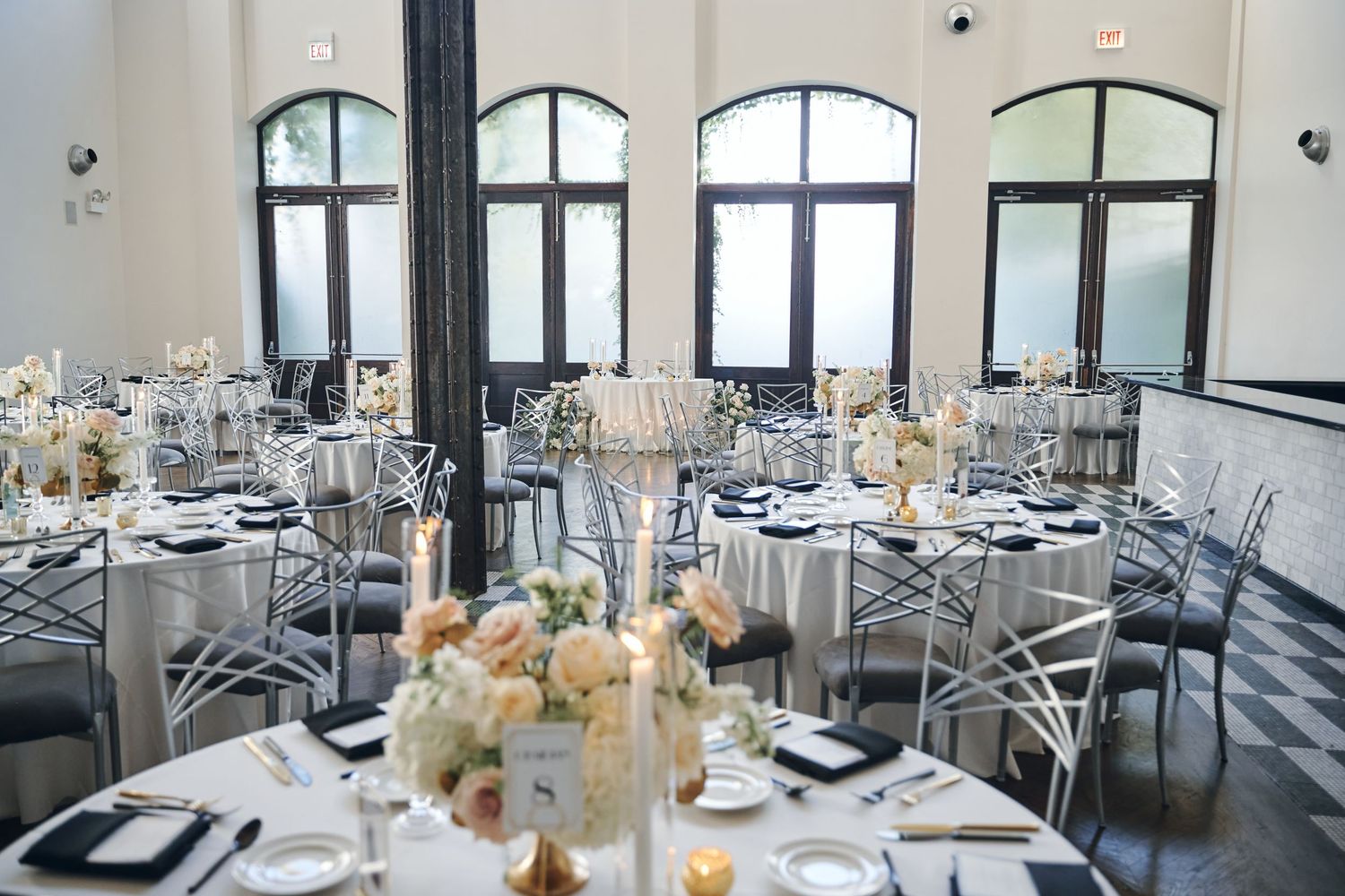 Elegant wedding reception tables set with white linens, floral centerpieces, and crystal chandeliers in a modern venue.