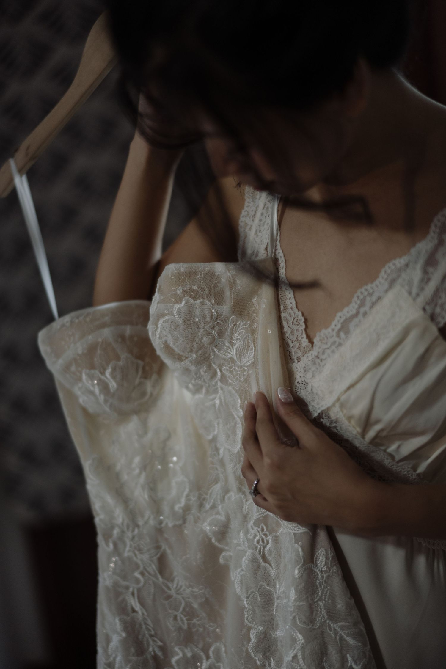 Close-up of a bride putting on her intricate floral lace wedding dress with spaghetti straps.