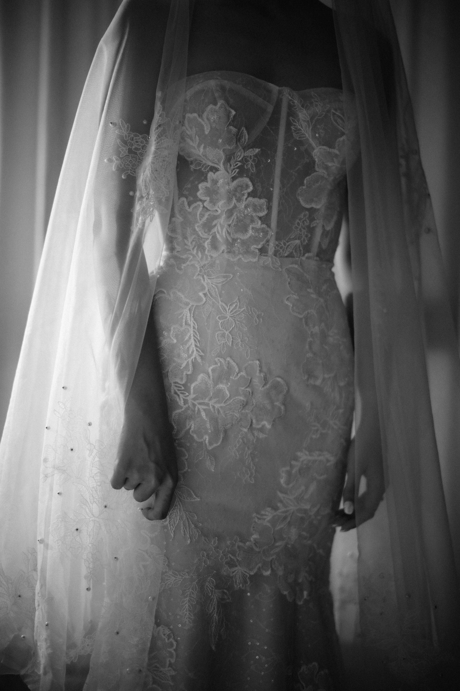 Black and white close-up of a bride in a fitted floral lace wedding dress with a flowing veil.