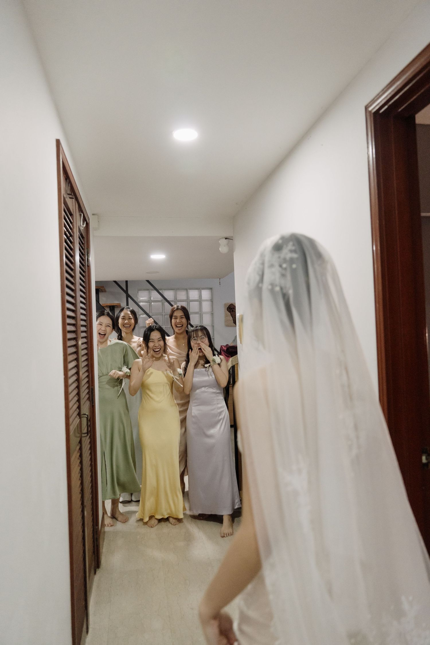 Bridesmaids in colorful dresses react with excitement as bride reveals her wedding look.