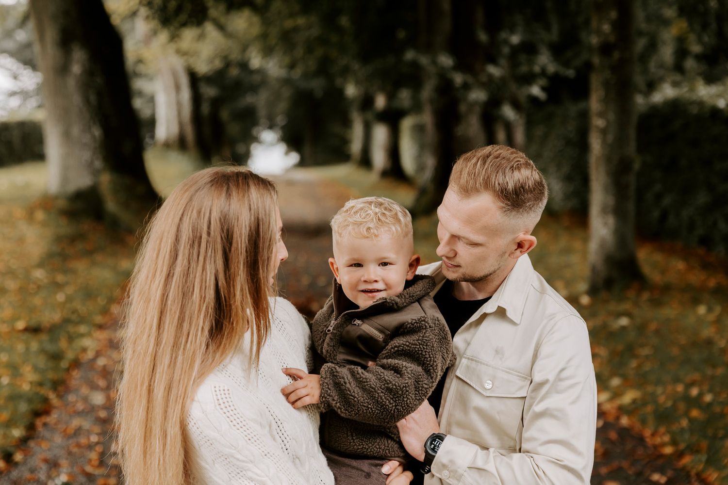 Familie, der deler et intimt øjeblik på en træallé om efteråret med faldne blade. Fotograf Middelfart