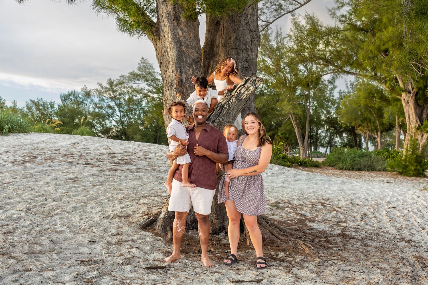 Family posing together on rocky beach at sunset with waves and colorful sky in background. Bradenton Florida Lifestyle Photographer