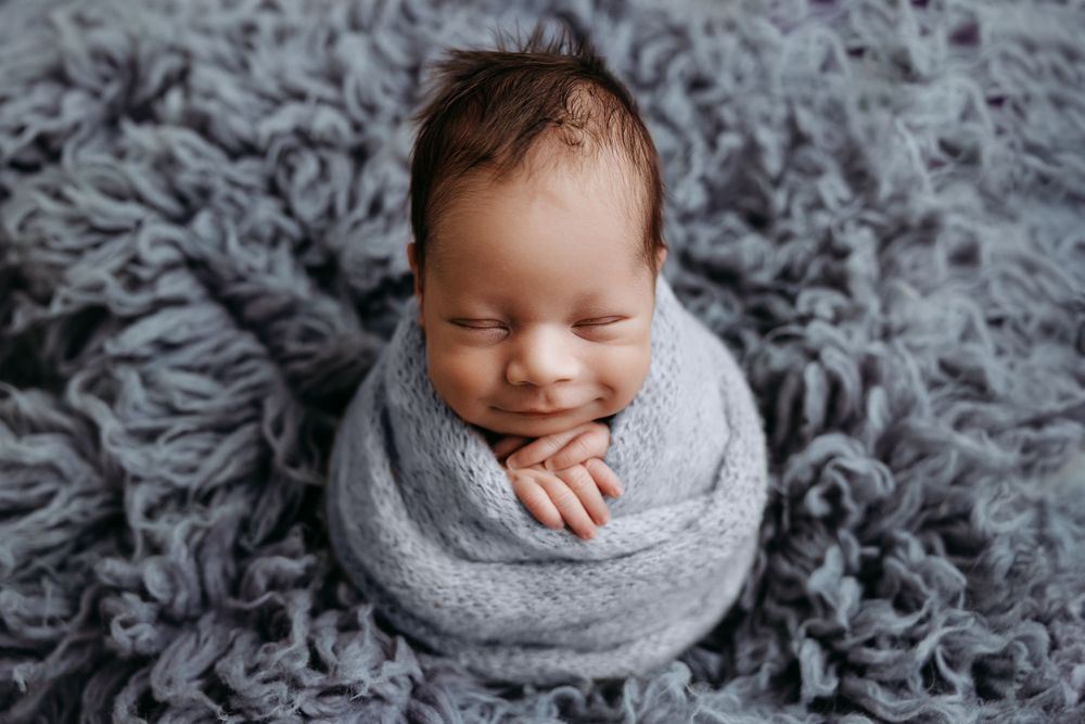 Newborn baby sleeping peacefully on soft gray textured blanket in professional studio setting.