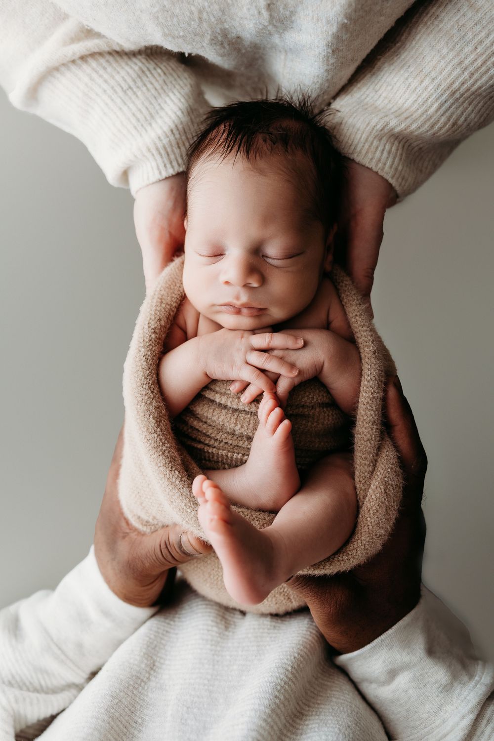 A peaceful sleeping newborn baby wrapped in cozy beige blankets lies on white bedding in a minimalist setting.