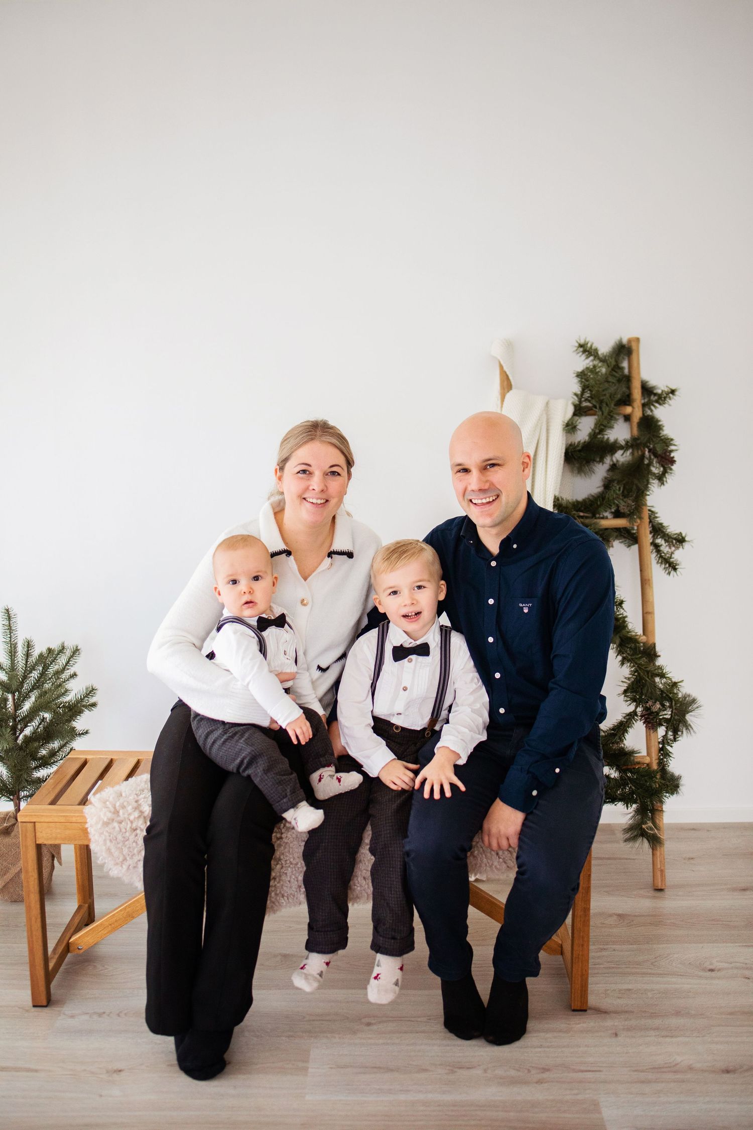 En familj poserar tillsammans i koordinerade formella kläder mot en minimalistisk bakgrund med julgranar.
