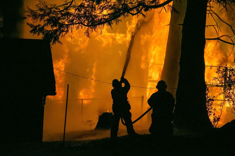 Silhouettes of firefighters battle intense orange flames in nighttime forest fire.