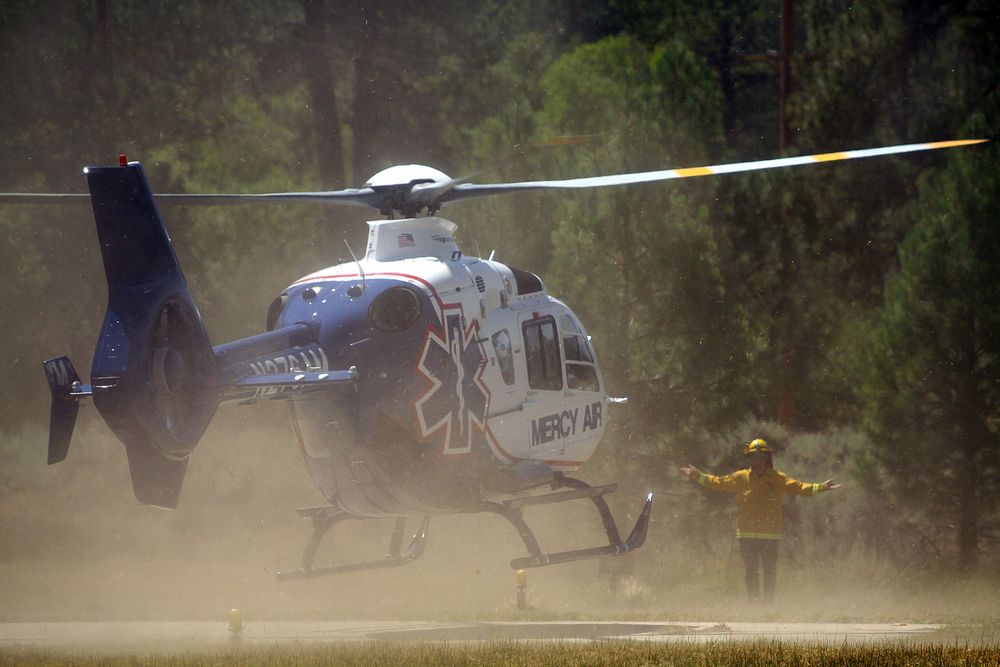 Emergency helicopter lands near firefighter during forest fire response operation.