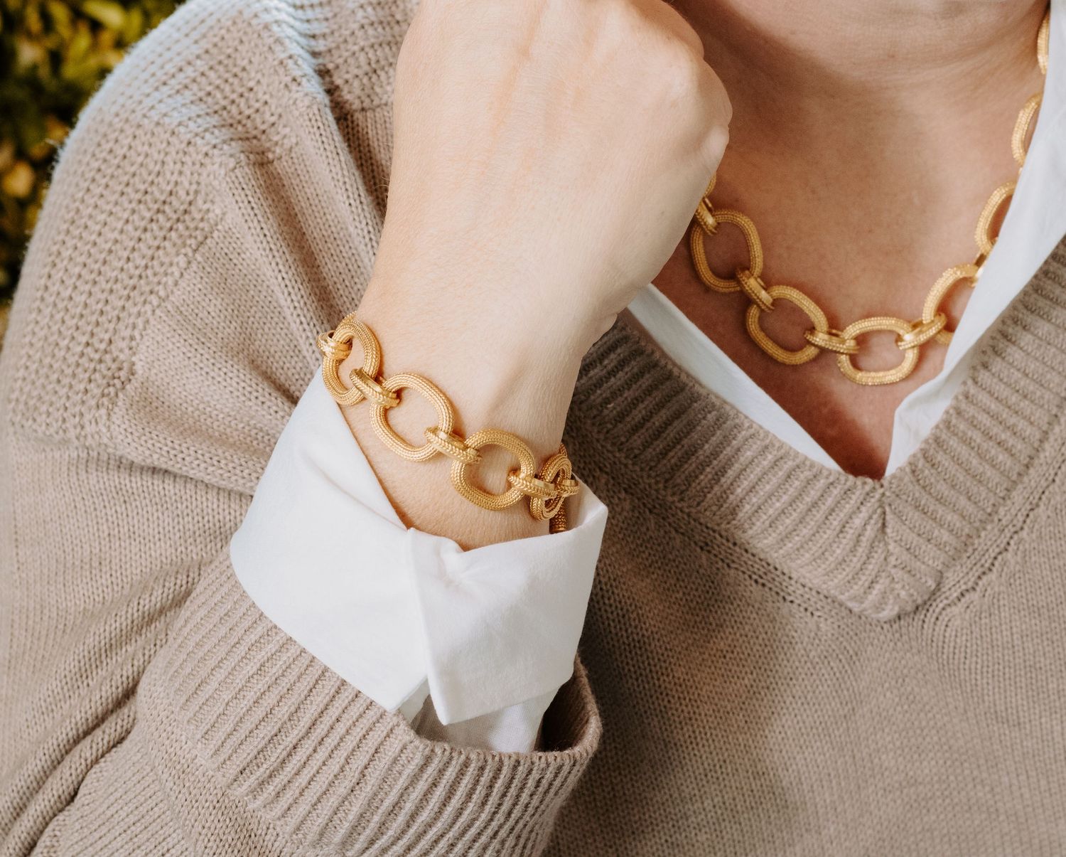 Model wearing matching gold Julie Vos, chunky chain link bracelet and necklace set with a beige knit sweater.