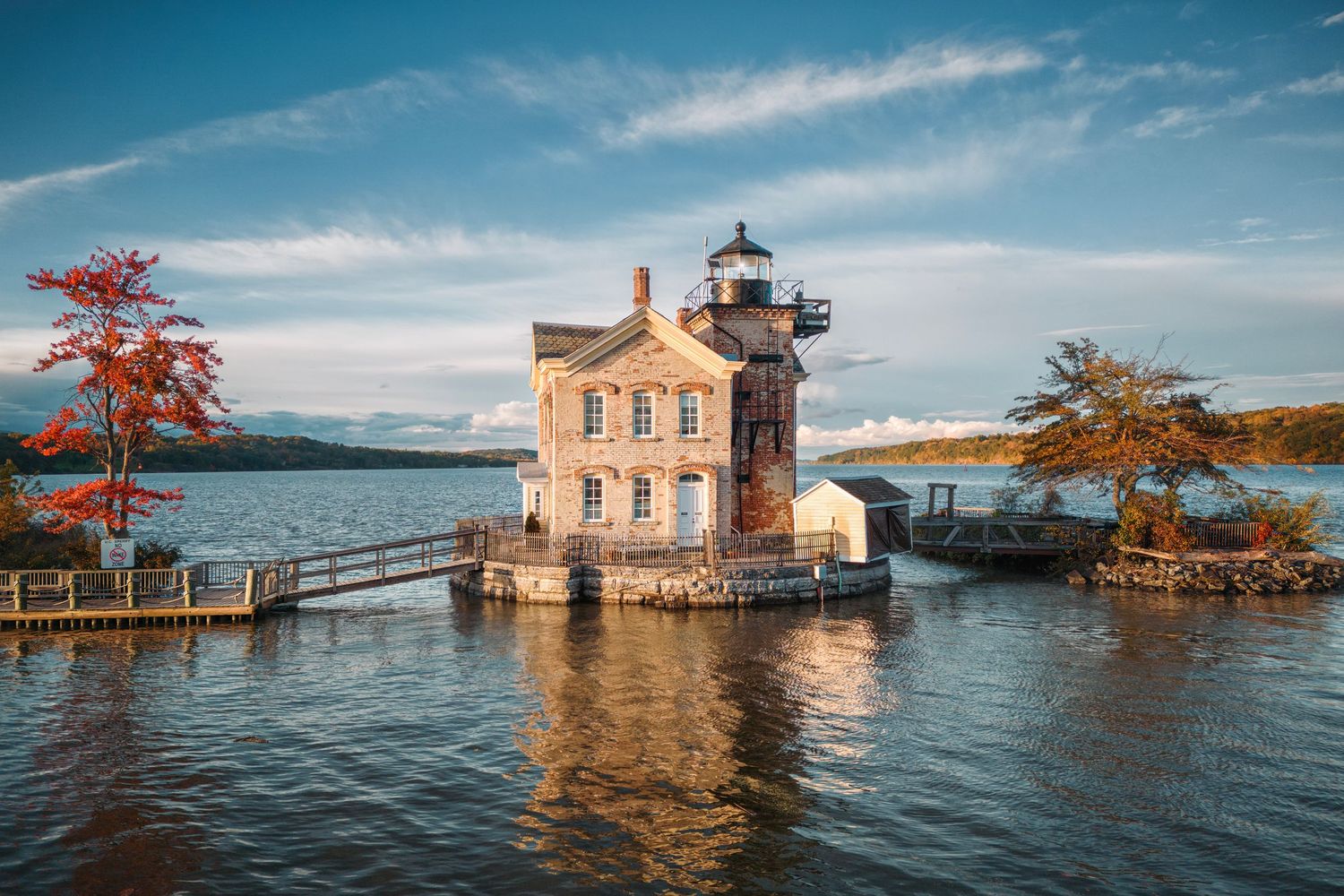 Historic lighthouse building surrounded by floodwaters and autumn trees under a blue sky with wispy clouds.