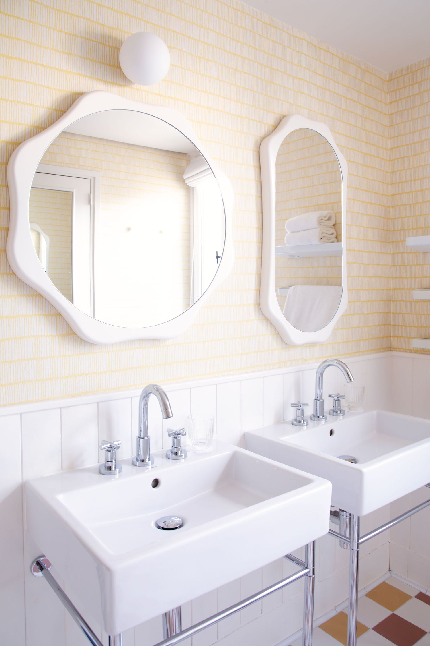 Modern white bathroom interior with curved mirrors and sleek rectangular sinks mounted on a pale yellow tiled wall.