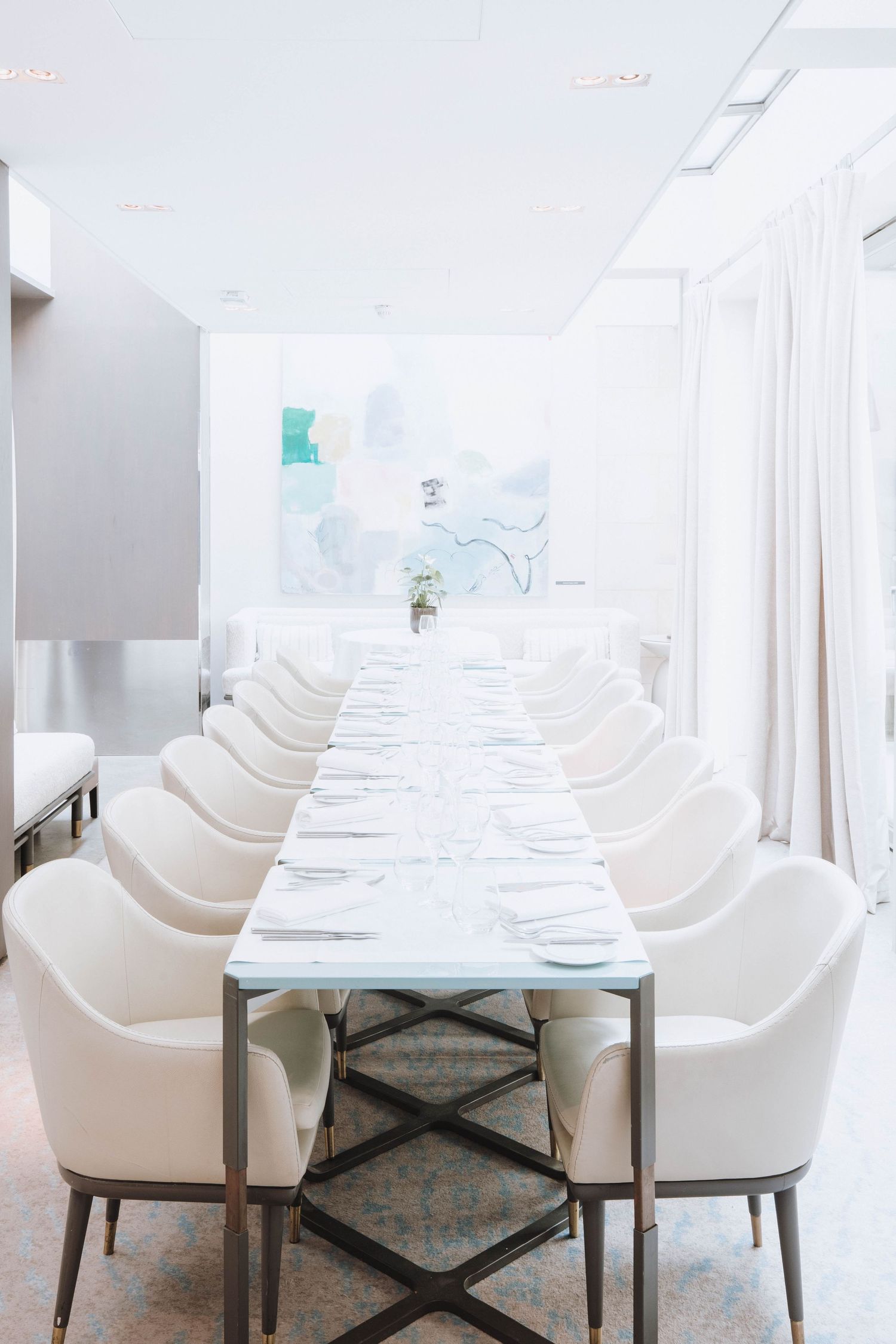Modern white dining room interior with plush chairs and tables arranged in a row, creating an elegant restaurant setting.