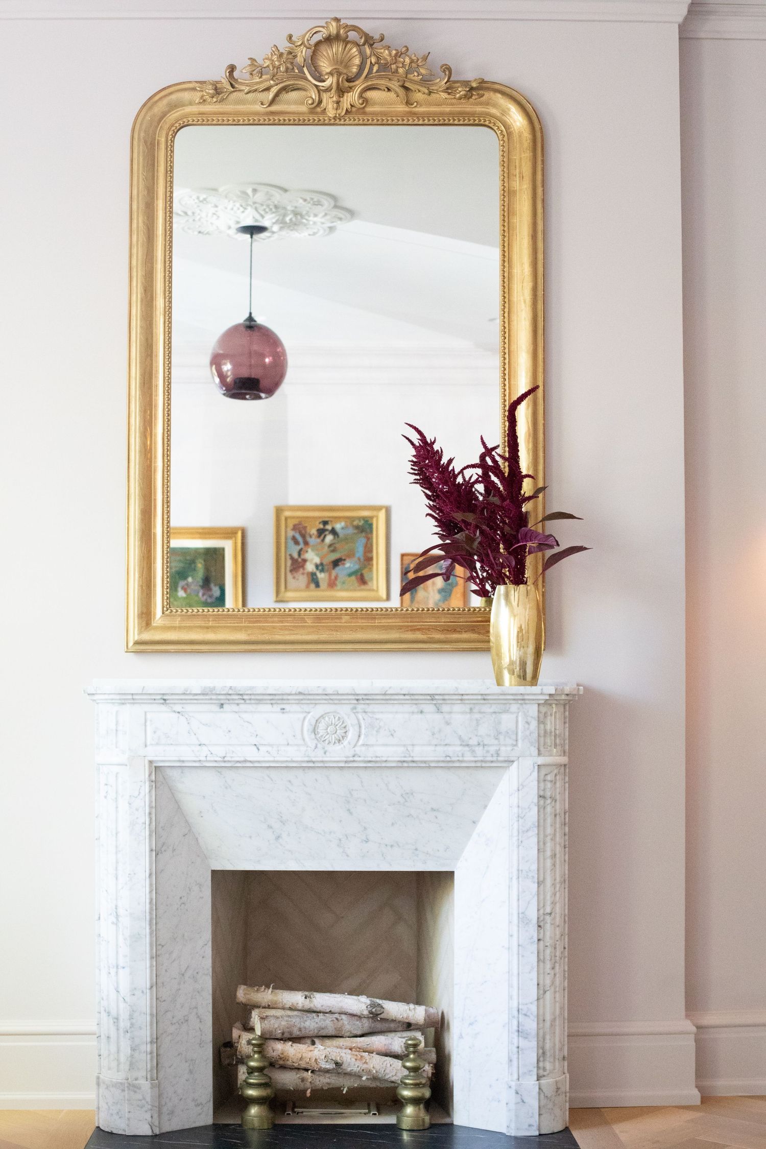 Elegant white fireplace mantels with ornate gold mirrors and decorative elements in a bright modern interior space.