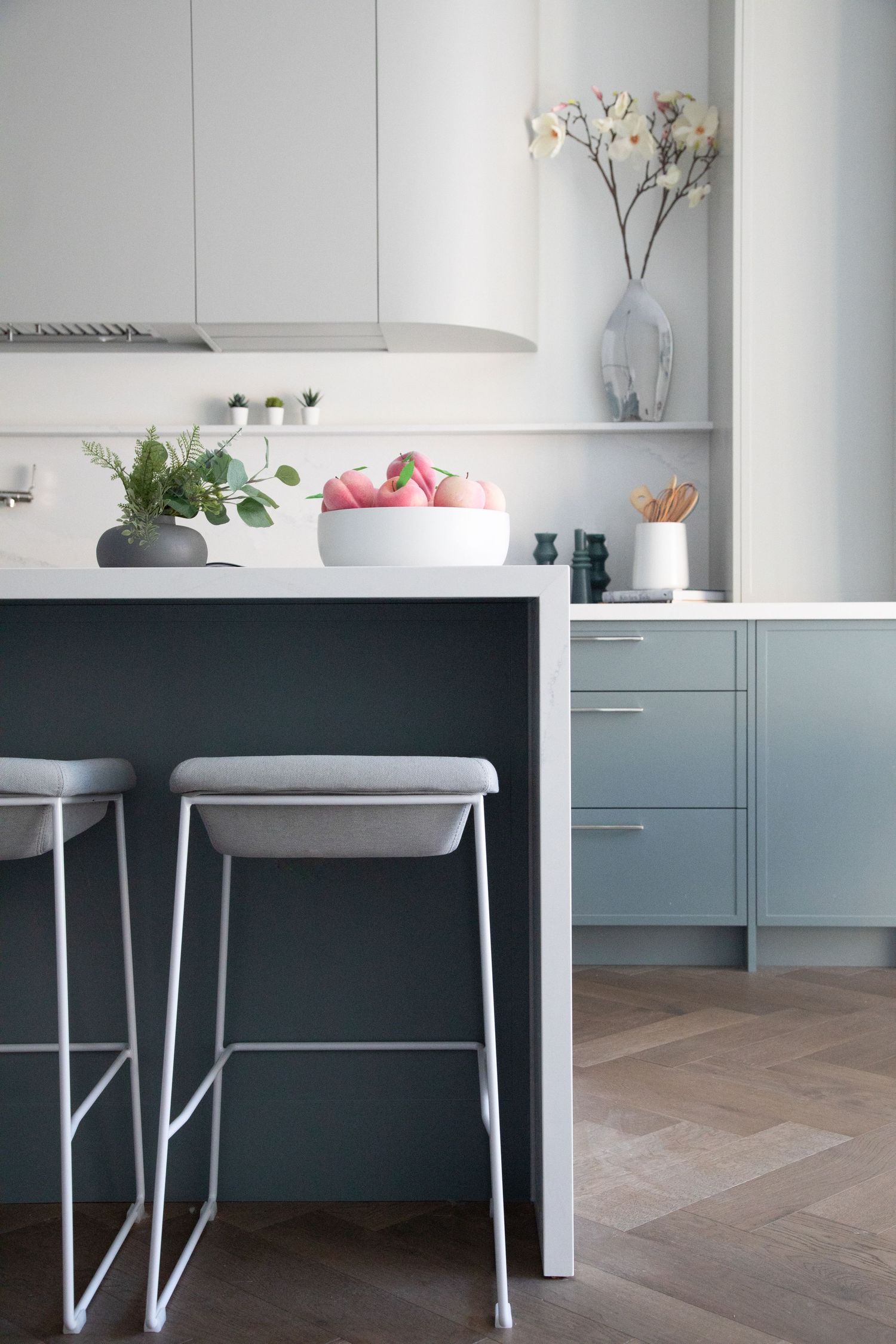 Minimalist white kitchen design with sleek cabinetry, built-in storage, and orchid decor on floating shelves.