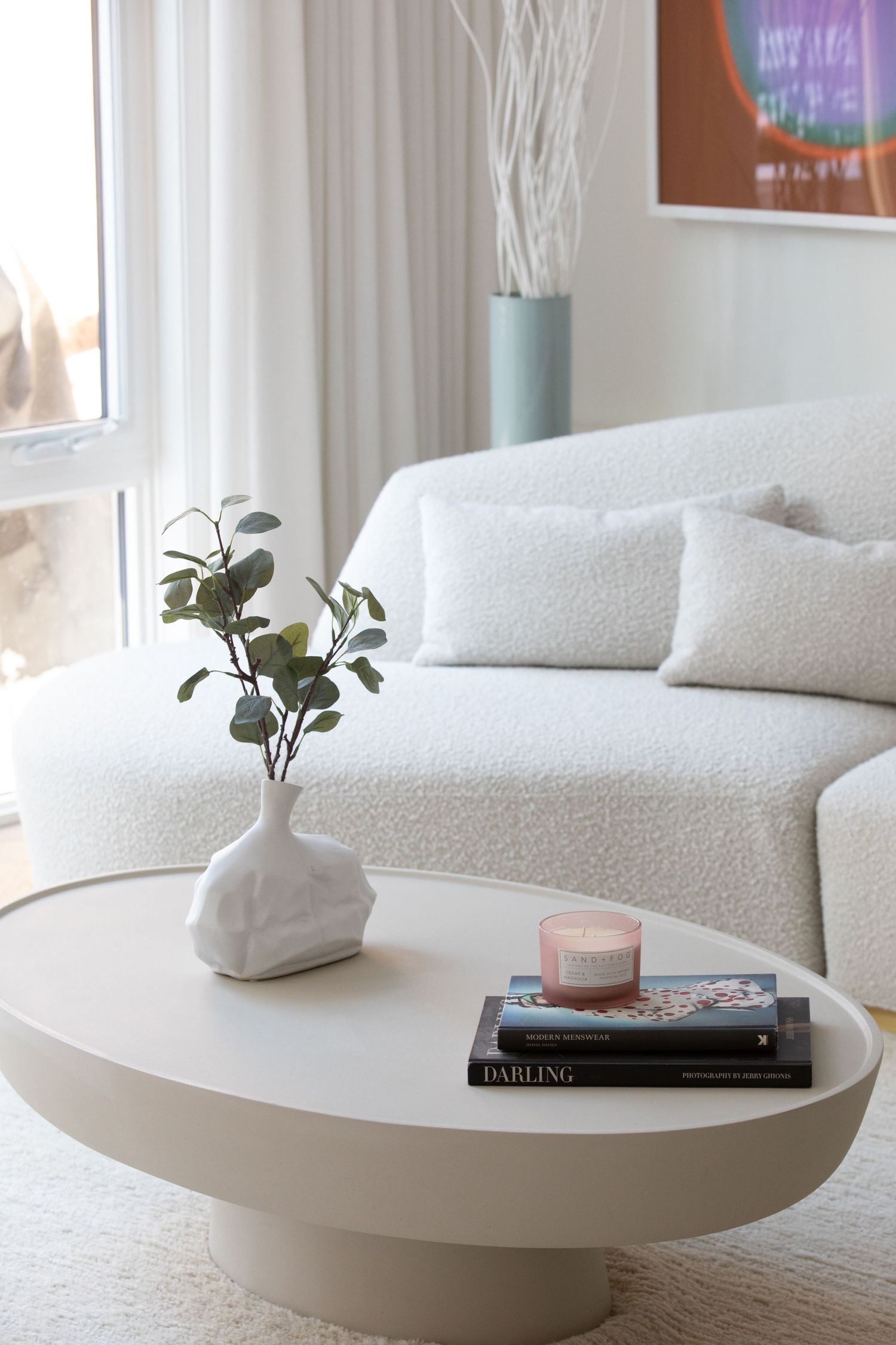 Modern living room with white curved sofa, round pedestal coffee table, and minimalist decor including vases and books.