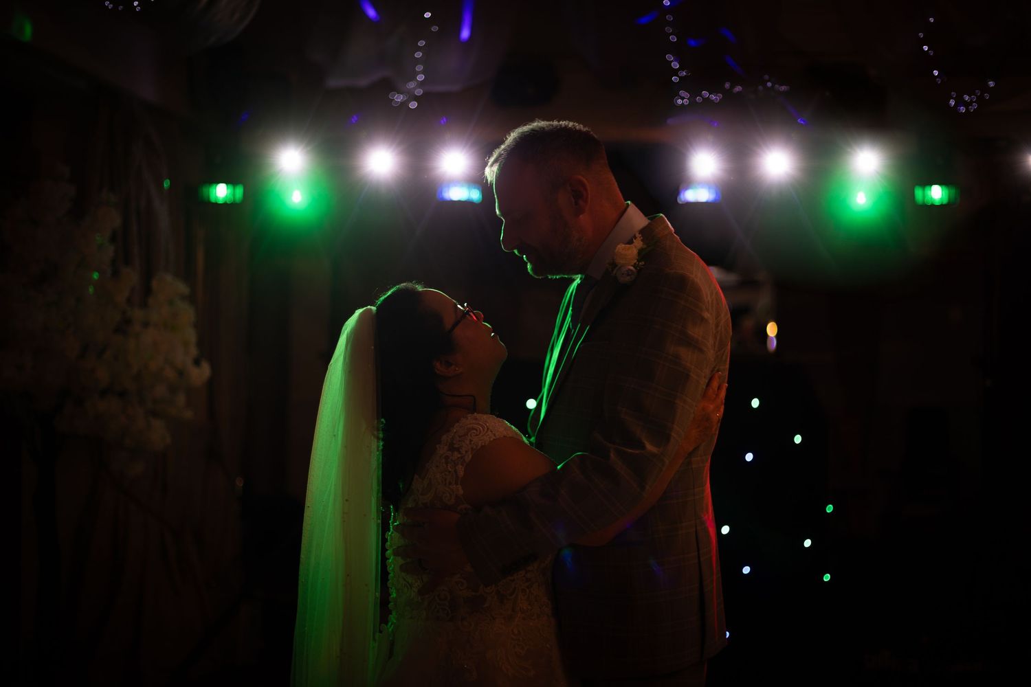 Bride and groom share romantic first dance under colorful green and white stage lights at elegant wedding reception.