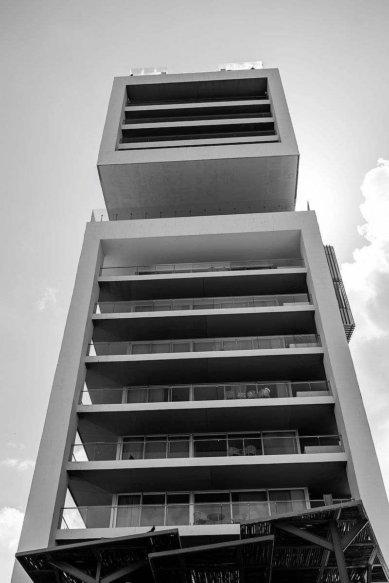 Black and white photo of a modern high-rise building with balconies shot from below against a cloudy sky at Dreams Vista Cancun.