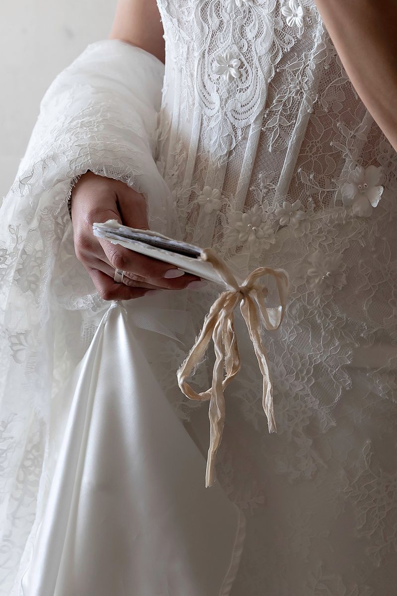 Bride in lace wedding gown holding a phone and satin ribbon bow detail on her dress.