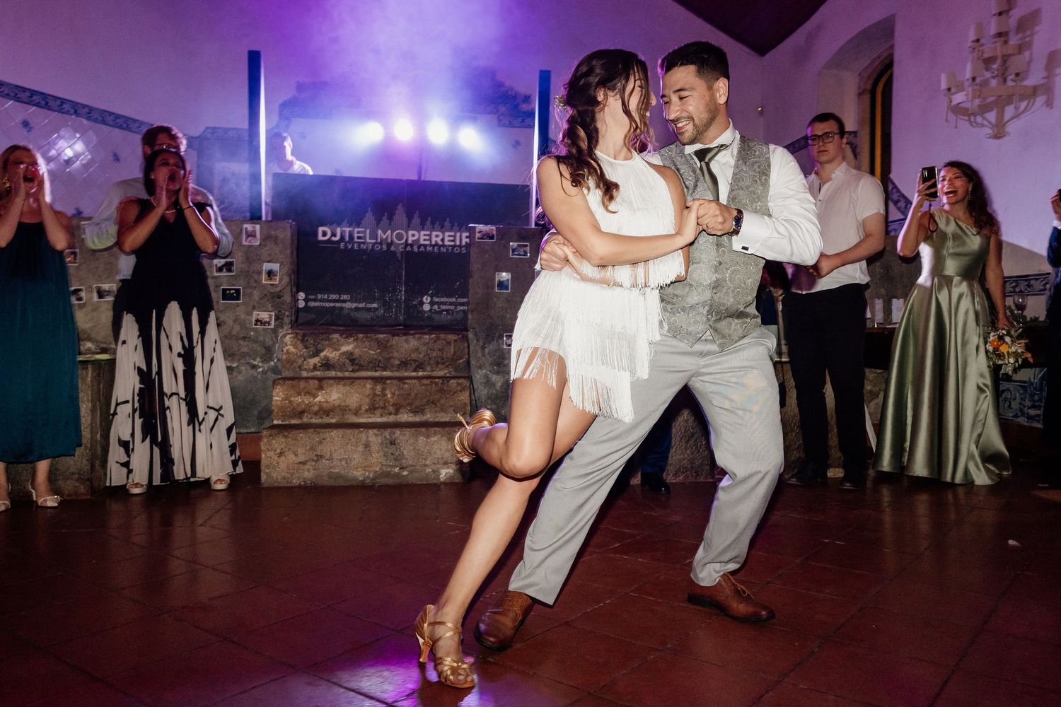 A couple dressed in formal attire dancing together on a dimly lit dance floor with other people in the background.