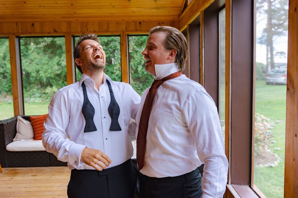 Two well-dressed men standing together and laughing in a rustic wooden building.