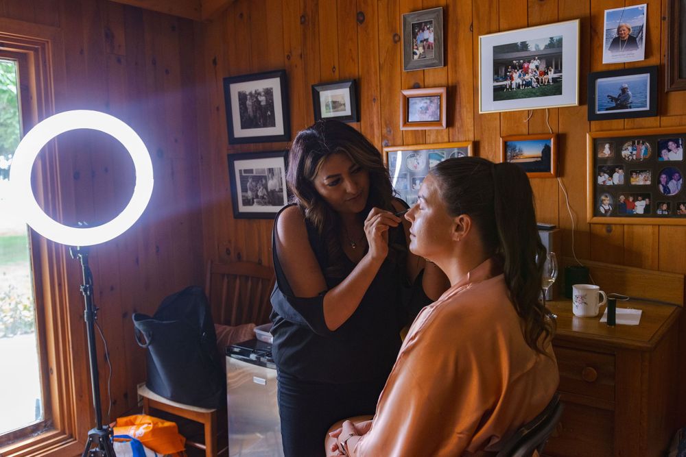 The image shows a woman applying makeup to another woman's face in what appears to be a home setting.