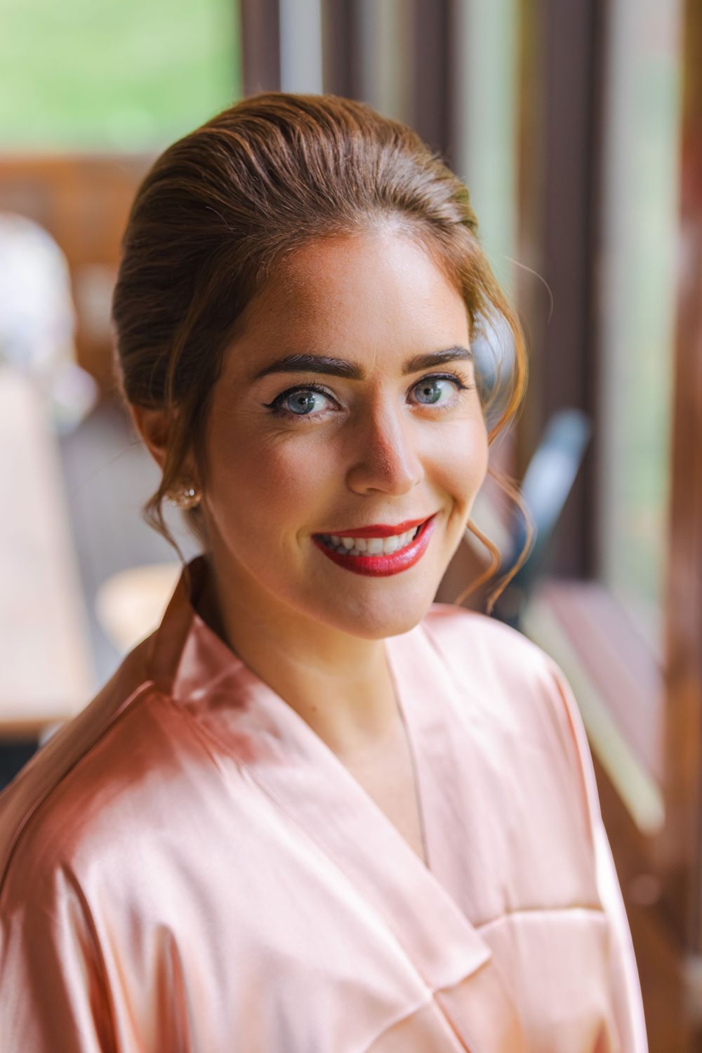 The image depicts a smiling woman with long brown hair wearing a pink robe against a blurred background.